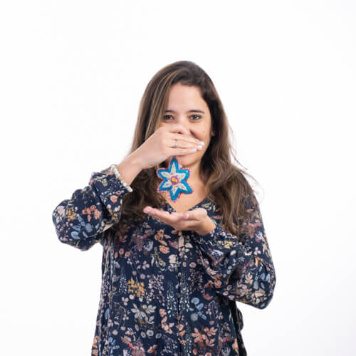 Photo studio de Claudia qui tient un porte clé en forme d'étoile qui brodé en laine colorée. Elle place ses mains comme si elle encadrait le porte-clé par le haut et le bas.
