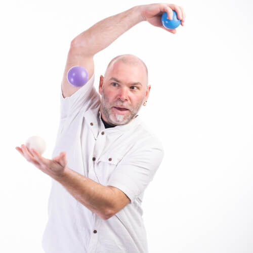 Photo studio de Steve qui jongle avec trois balles et il fixe la balle qui est au milieu dans le vide.