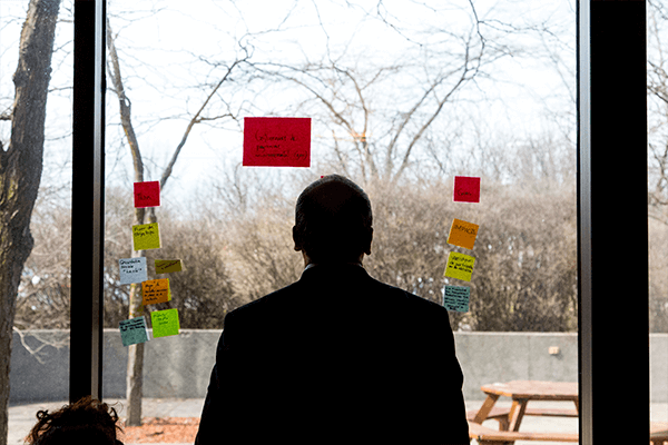 Photo d'une personne de dos devant une vitre avec plusieurs post-it en train d'analyser les notes prises